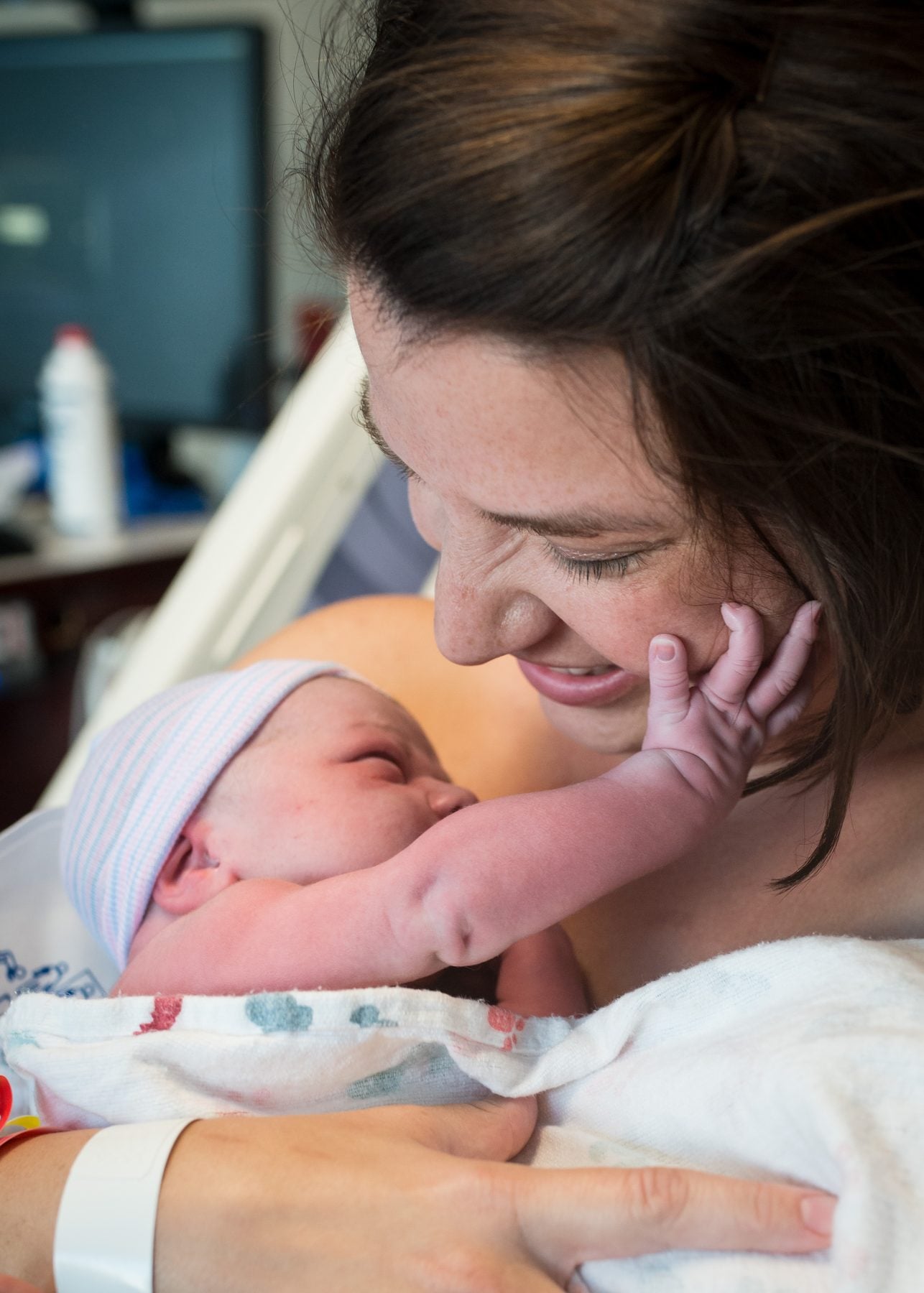 A mother smiling down at her newborn moments after delivery, the baby's hand resting against her cheek.