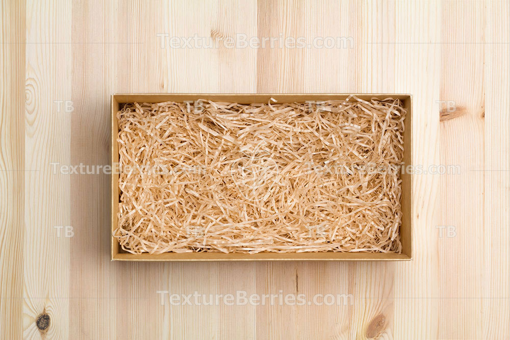 Gift box with decorative straw on wooden table, top view